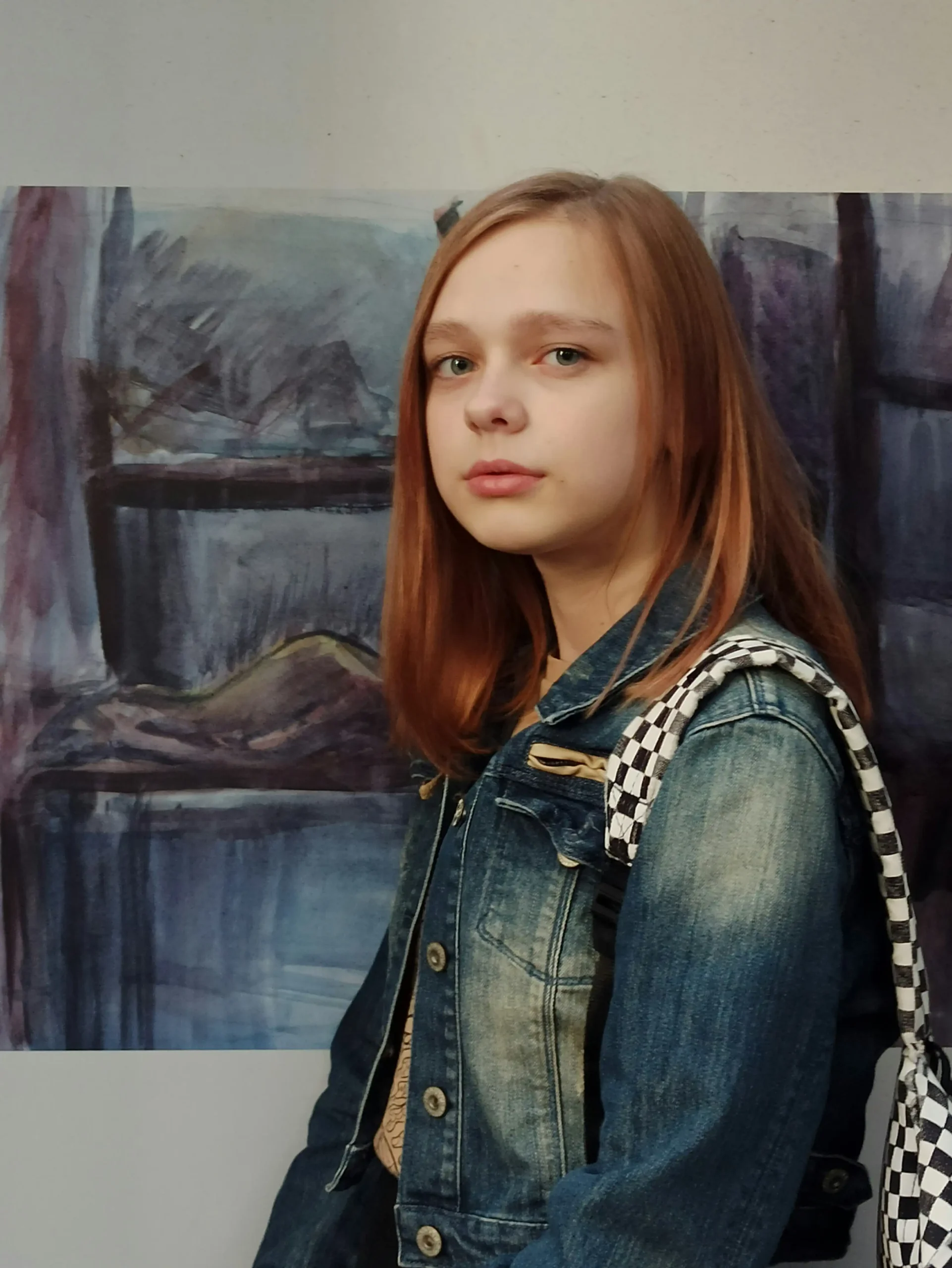 A teen girl in a denim jacket standing thoughtfully in front of a painting