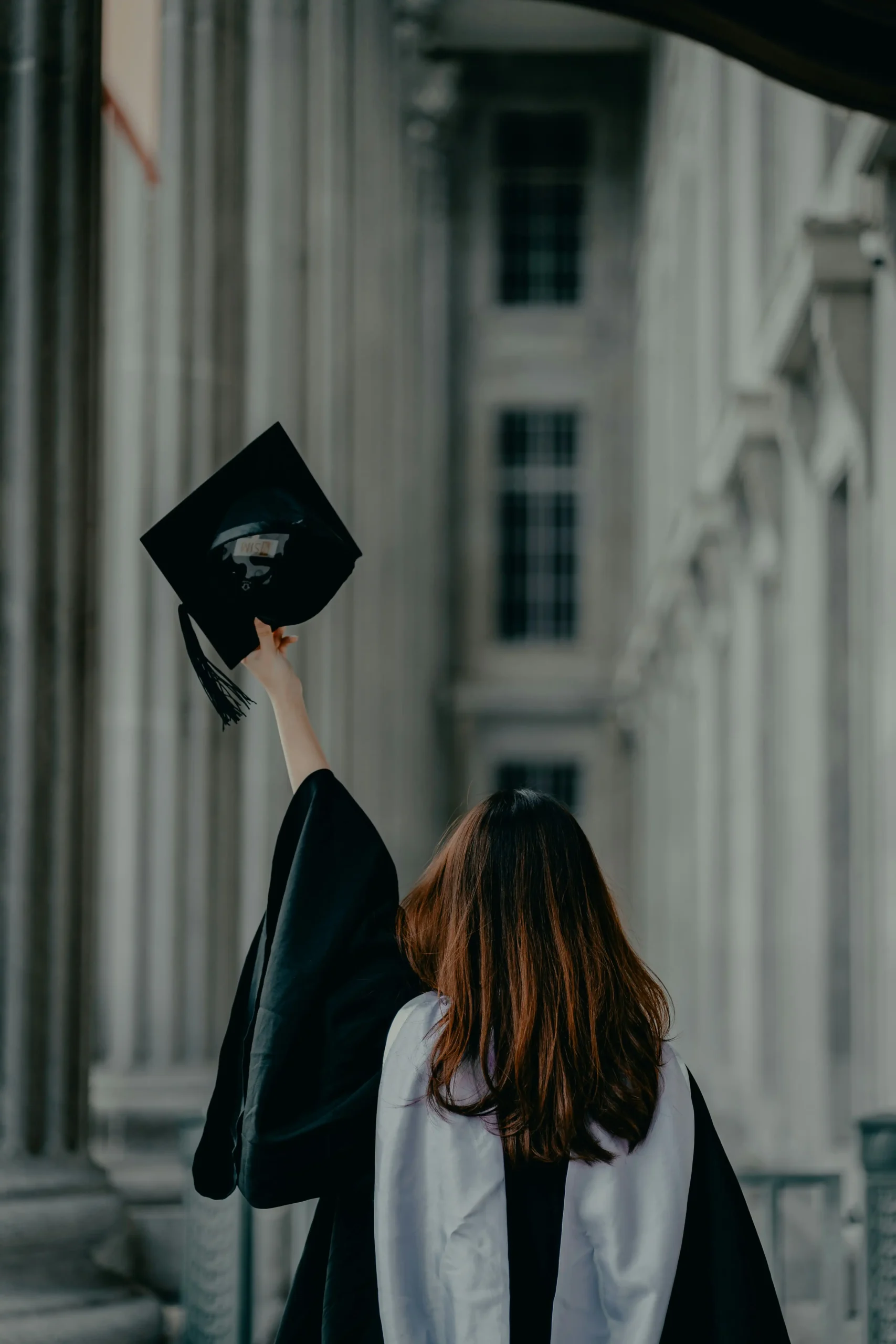A graduate holding a cap in front of an academic building