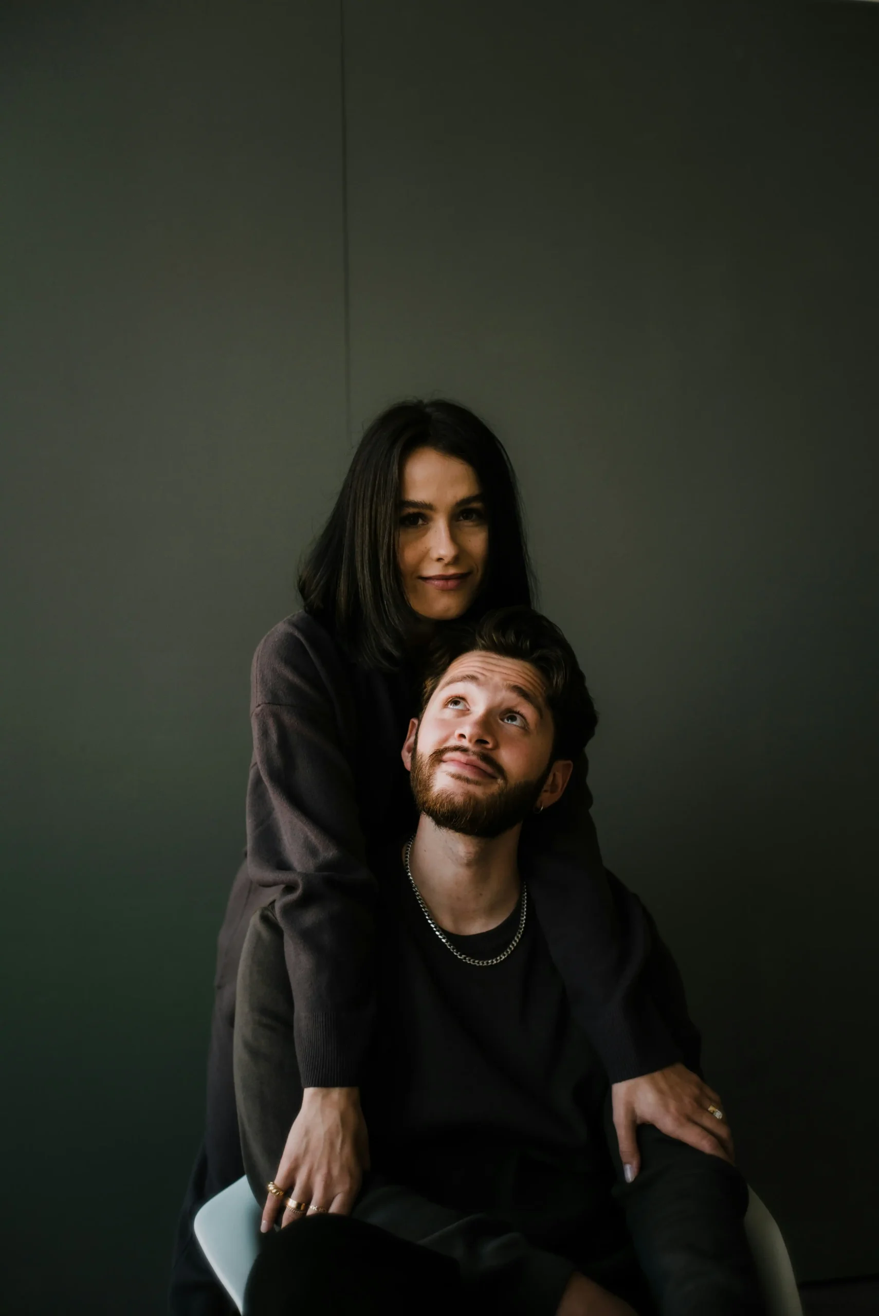 A woman standing behind a seated man, both smiling warmly at each other