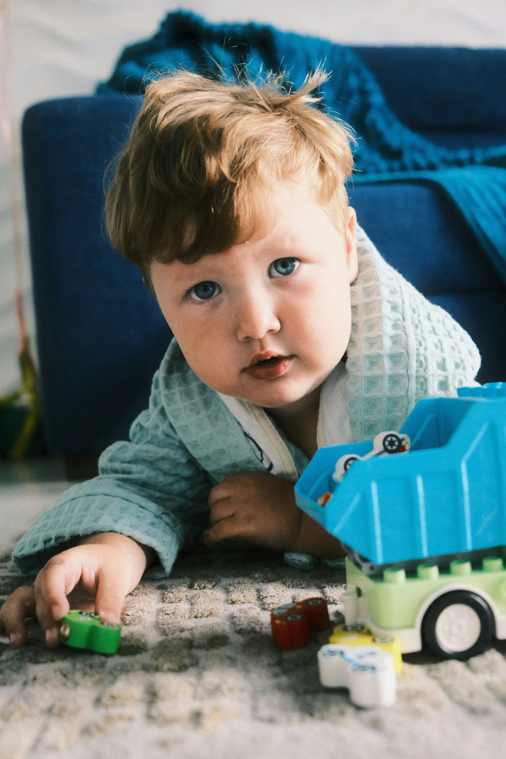 A toddler on the floor glancing up while playing with toy trucks