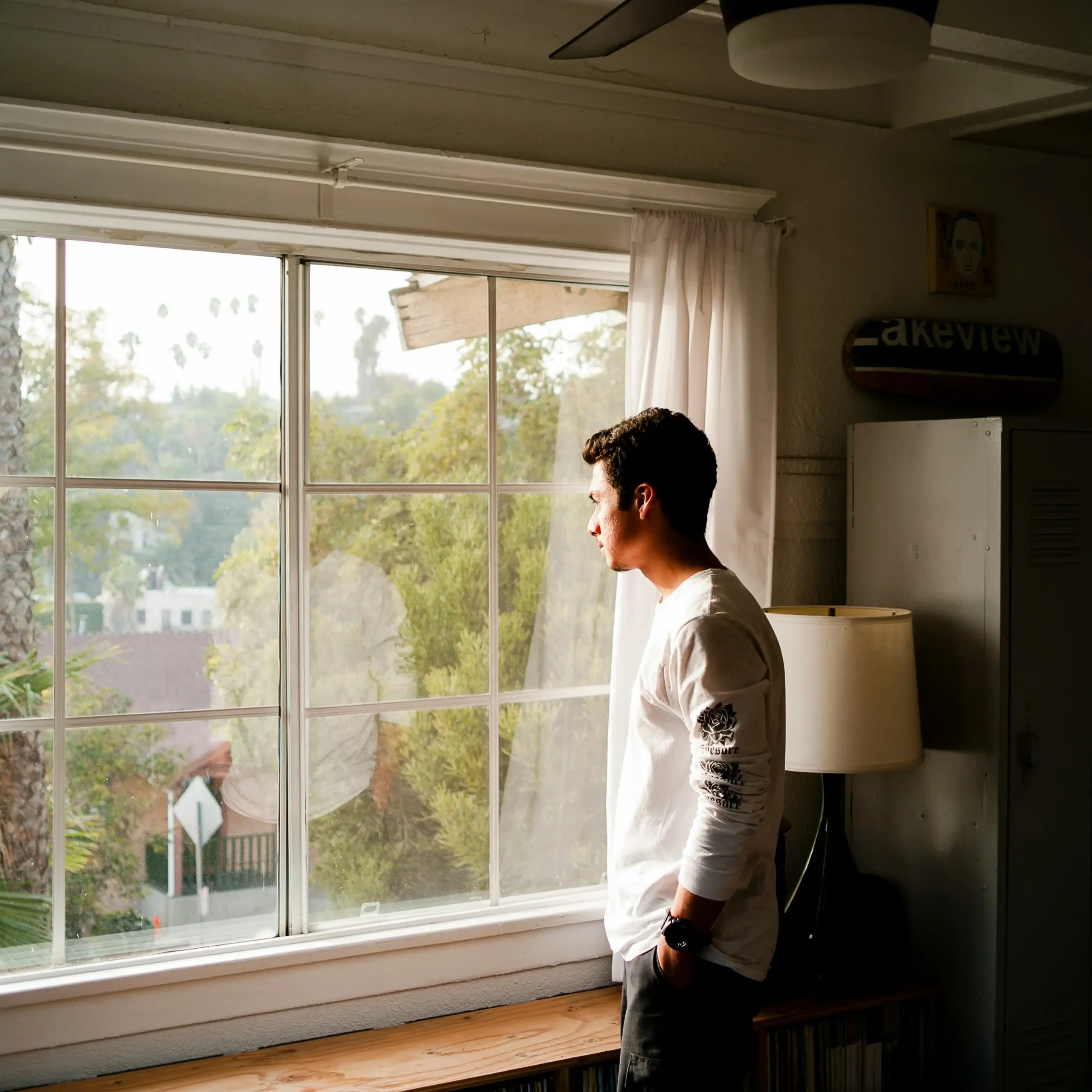 A young man standing alone, looking out a window