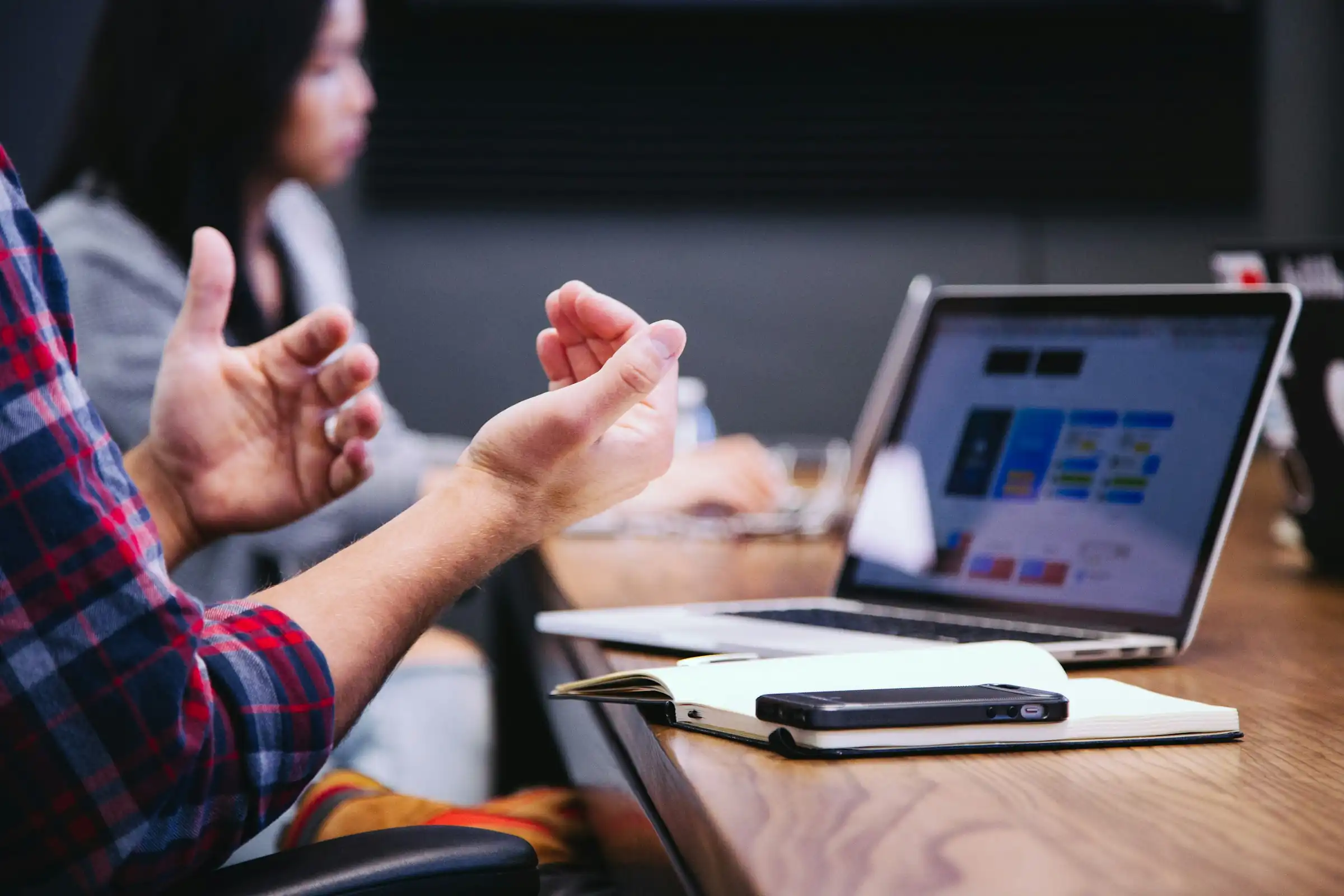 Two people gesturing during a supervision meeting with a laptop and notebook on the table