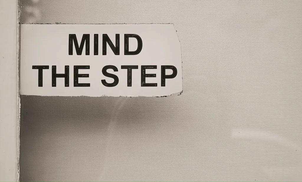 A torn paper sign reading 'Mind the Step' taped to a wall