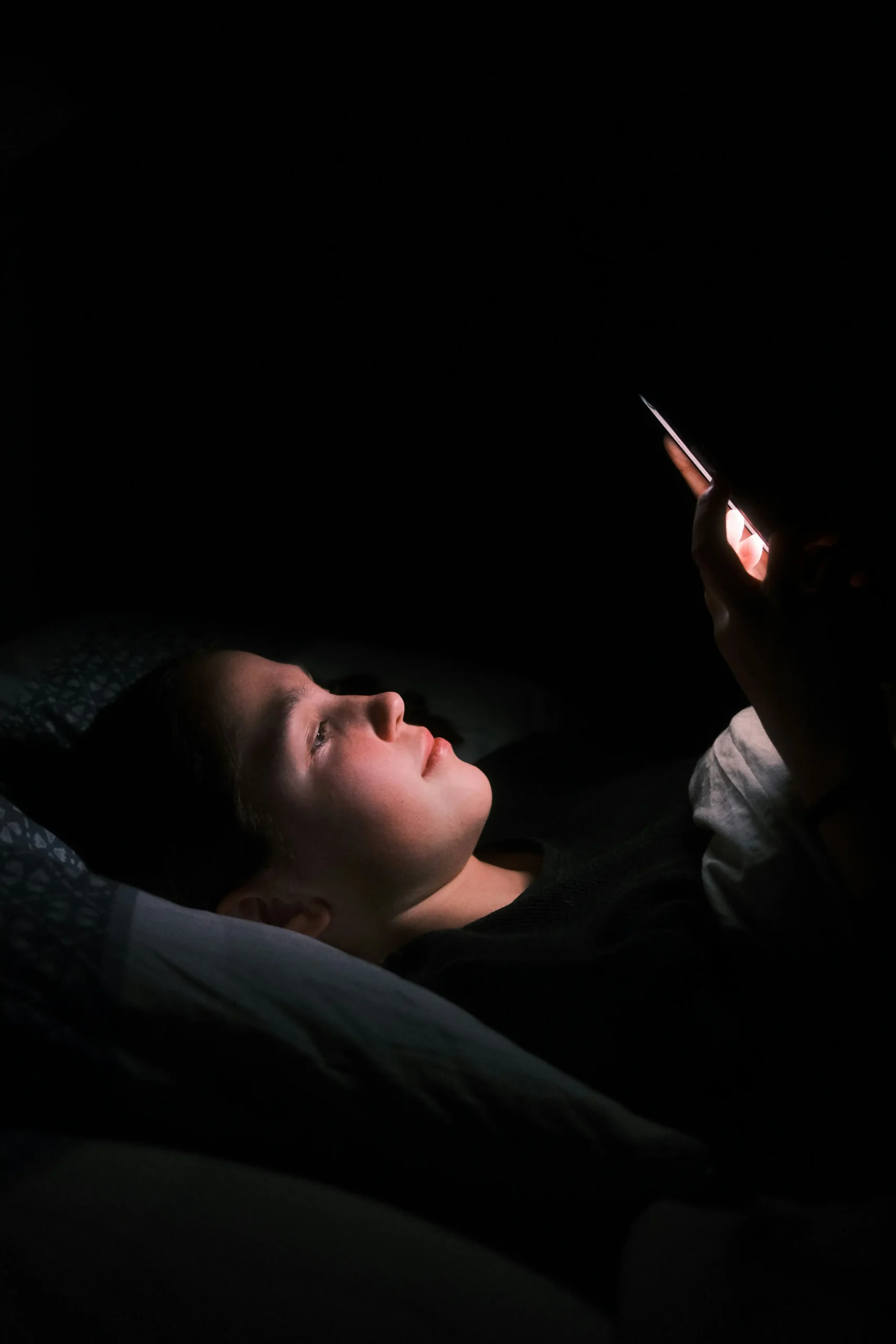 A woman lying in bed with the light from her phone glowing on her face at night