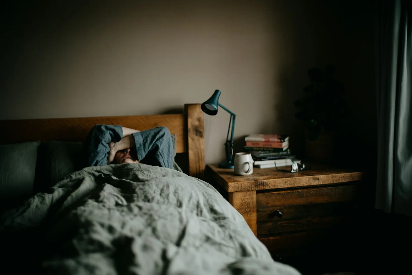 Man lying face-down under the covers in a dim, lived-in bedroom