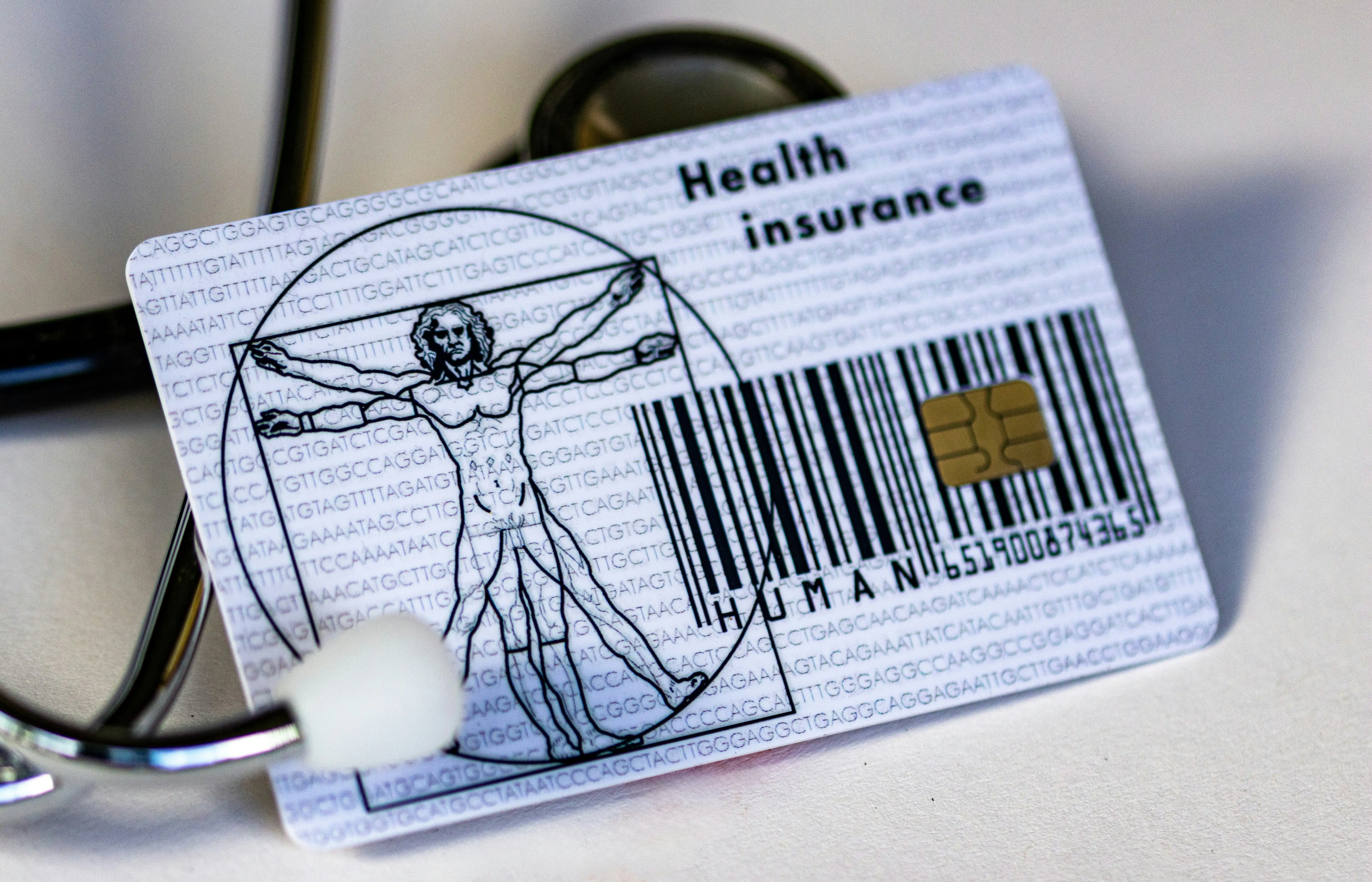 A mock health insurance card with a Vitruvian Man design and embedded chip, resting against a stethoscope