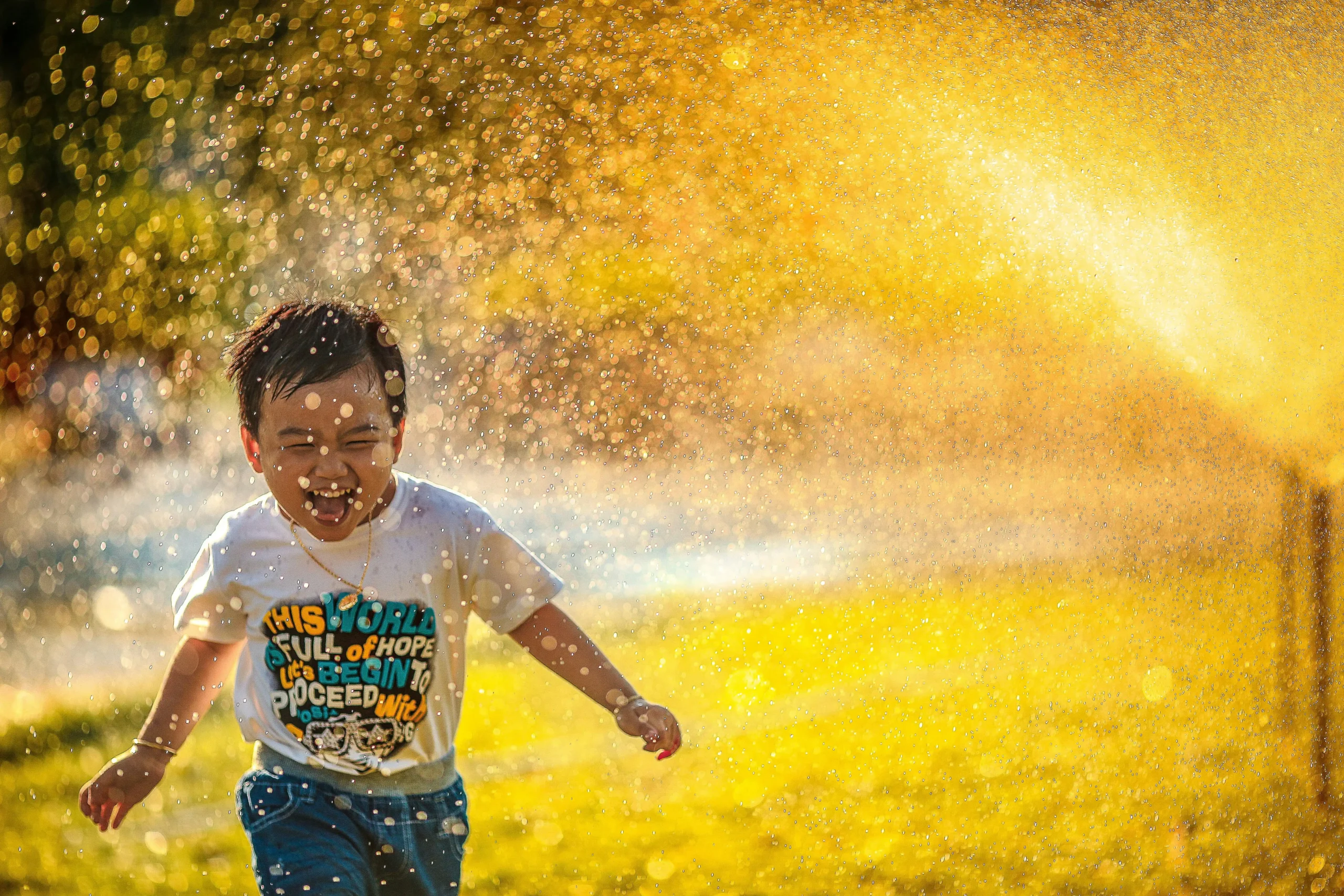 A laughing boy running through a sprinkler in golden afternoon light