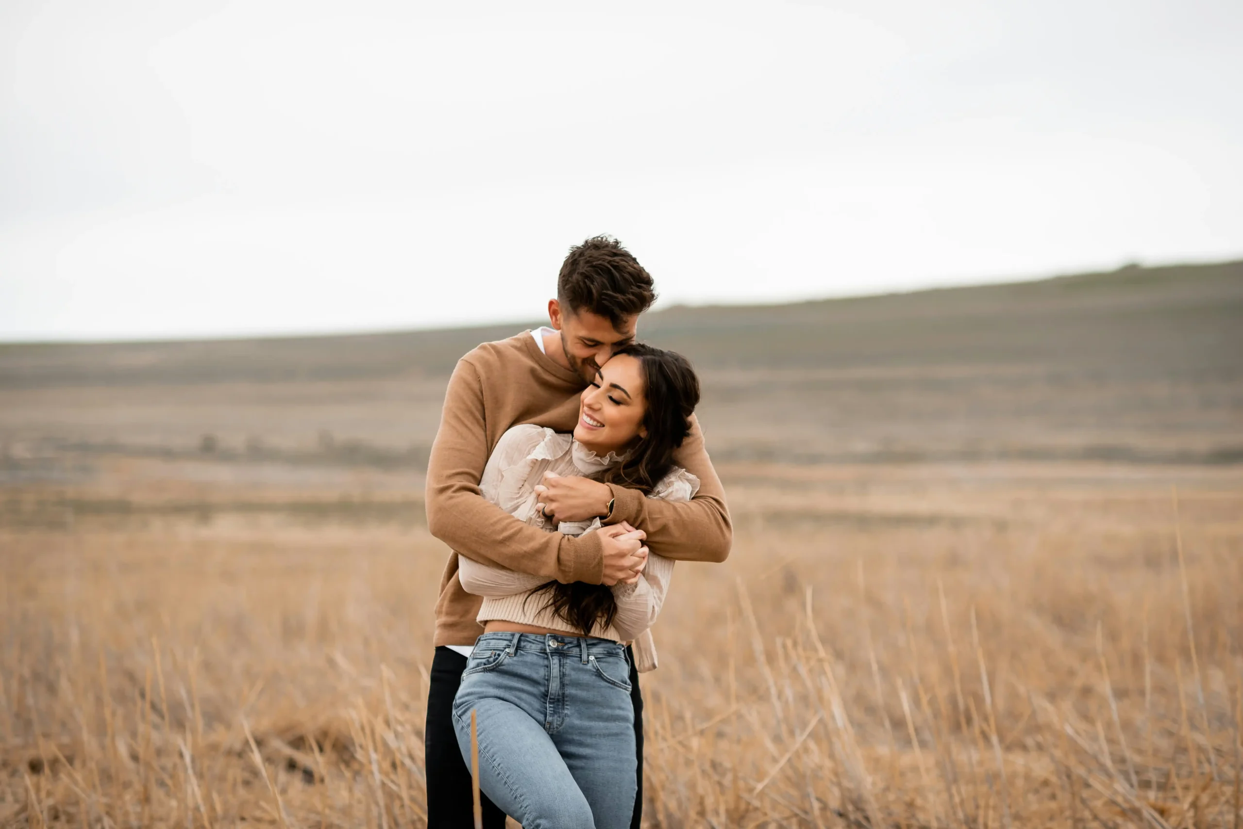 A couple embracing in a golden field, the man kissing the woman's forehead