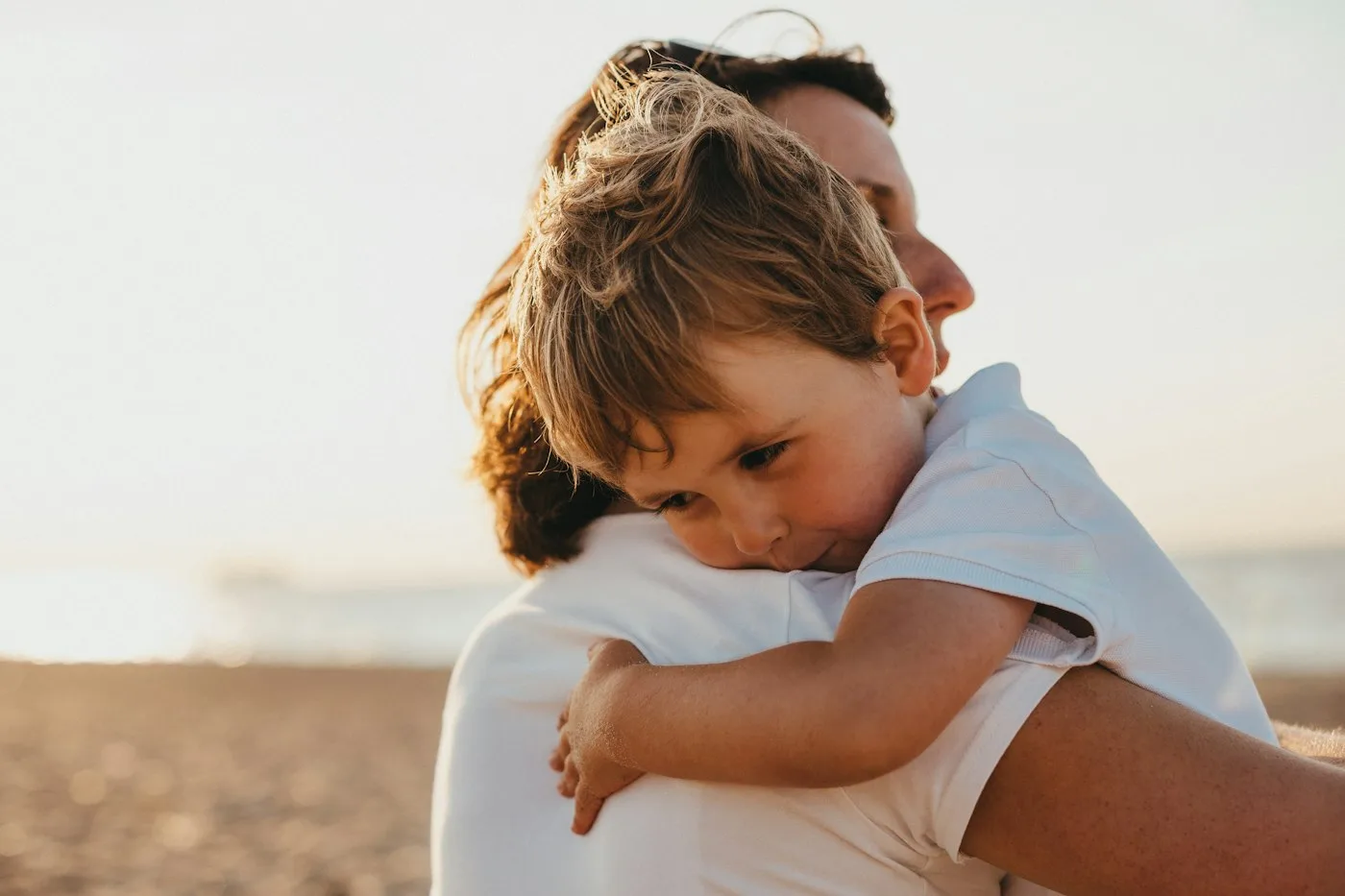 A parent holding a young child close on a beach at golden hour