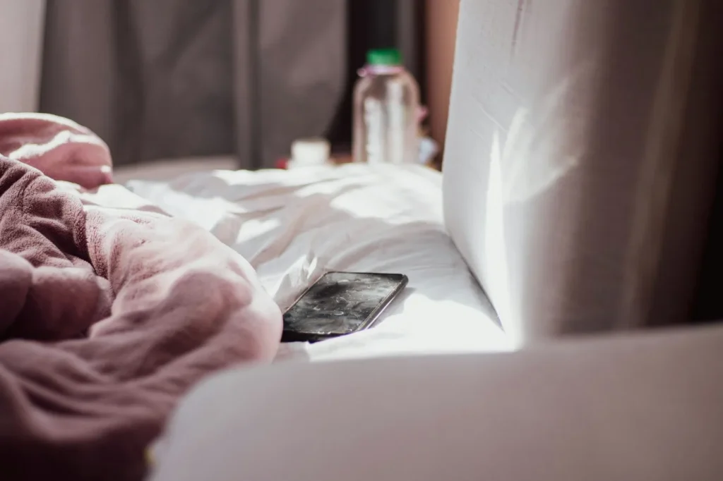 A phone resting on a rumpled, sunlit bed with no one in frame