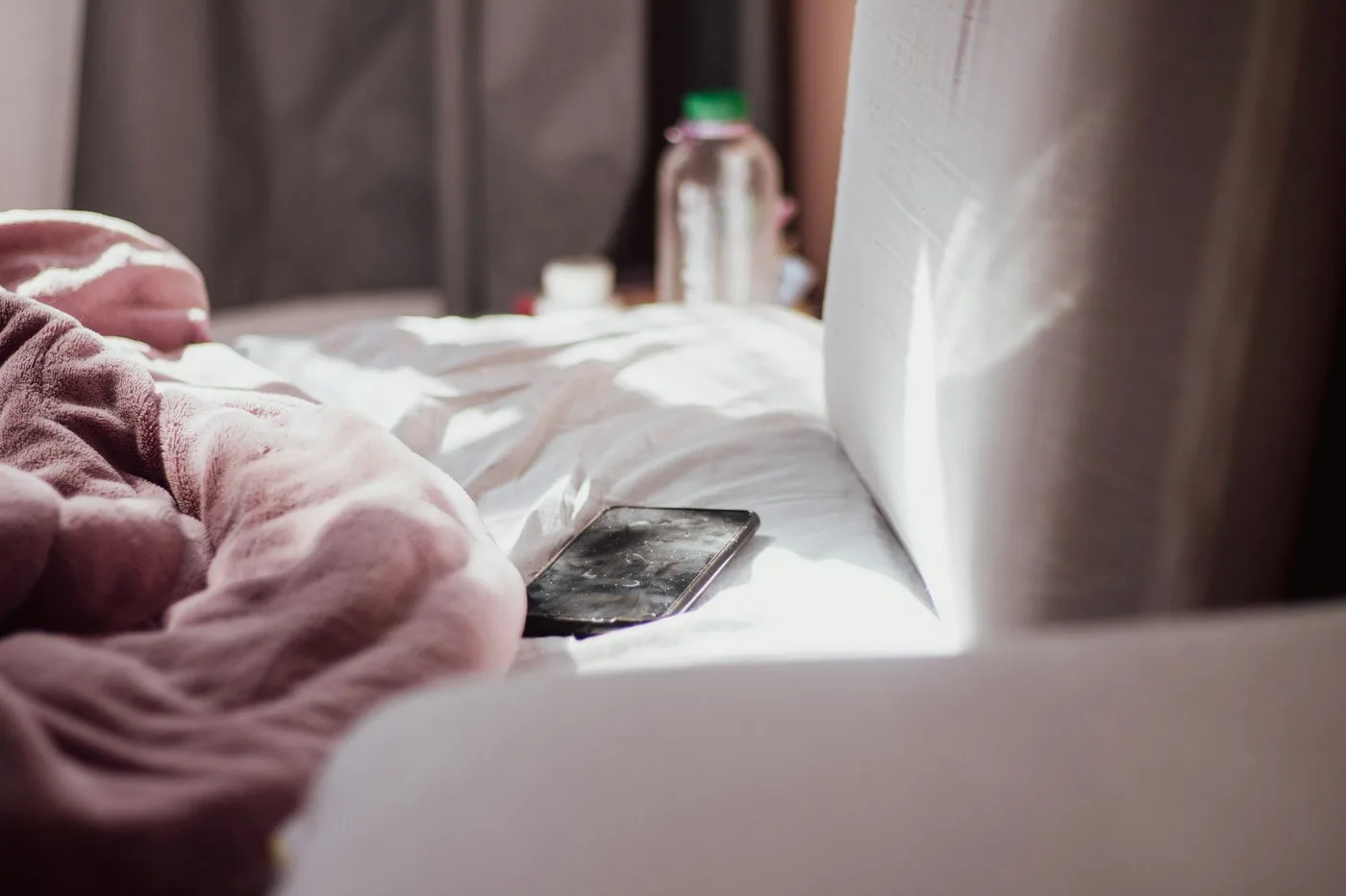 A phone resting on a rumpled, sunlit bed with no one in frame