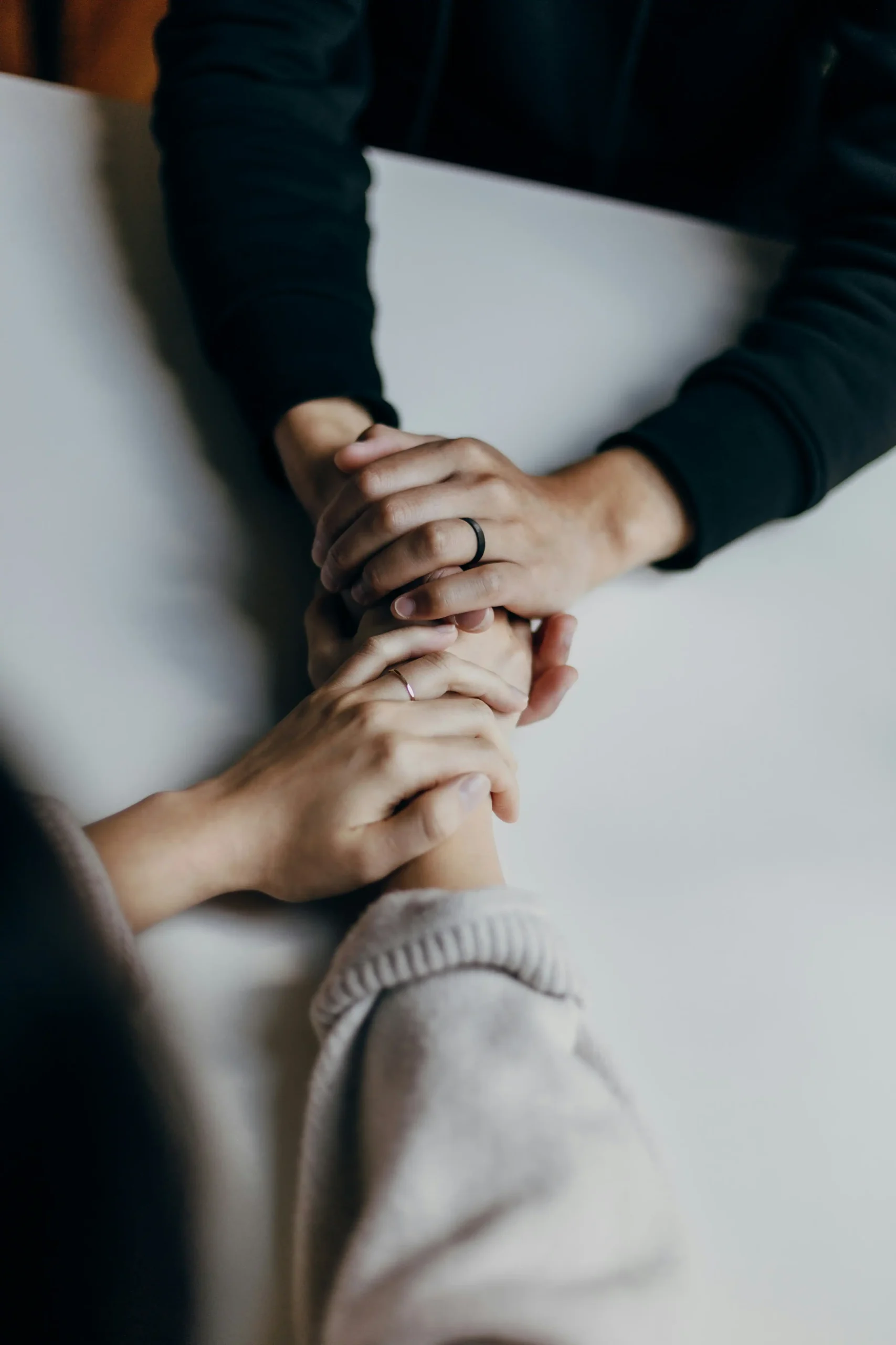 A couple holding hands across a table, both wearing wedding rings