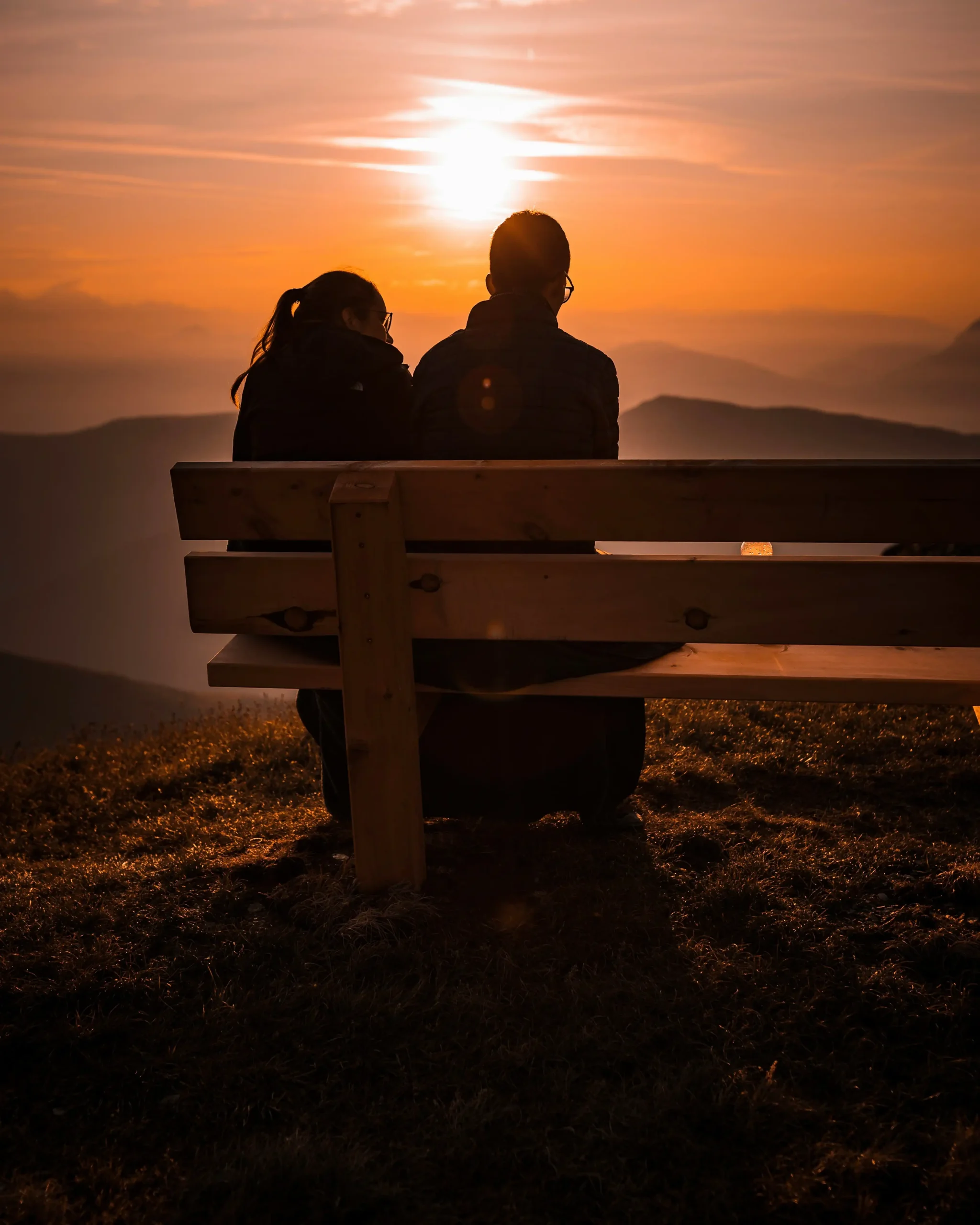 A couple sitting together on a bench, watching the sunset