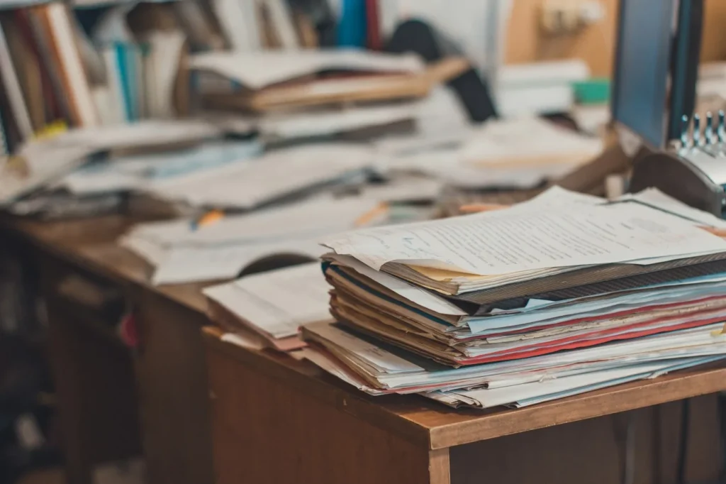 A tall stack of papers piled on a wooden desk