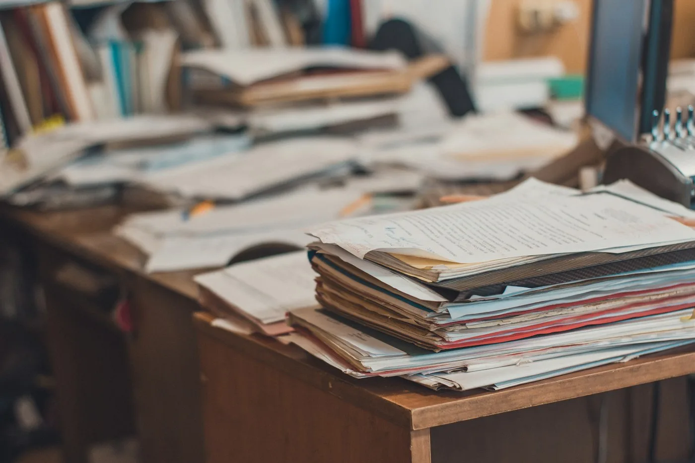 A tall stack of papers piled on a wooden desk