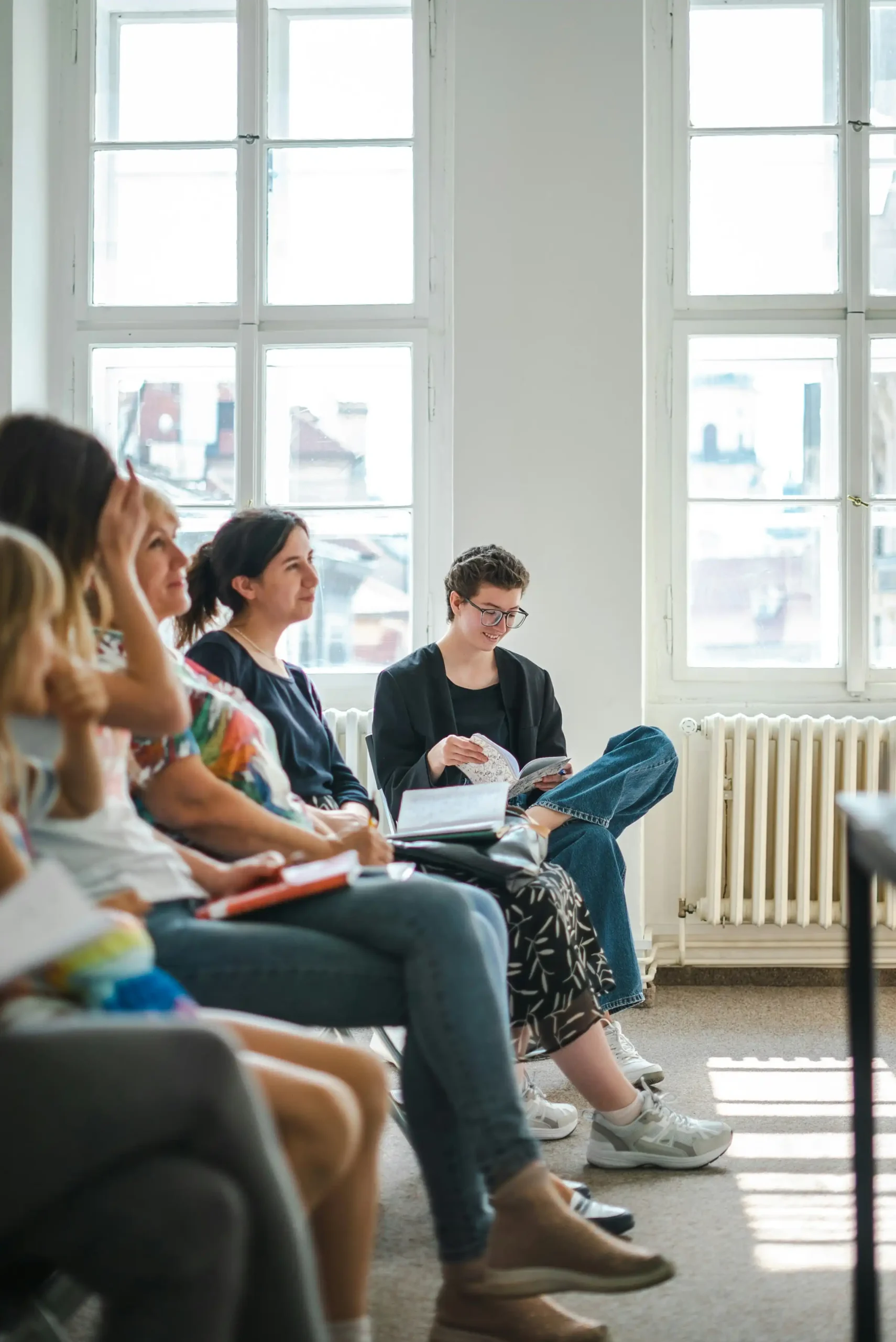 A group sitting in a circle with notebooks, listening and sharing during a group session