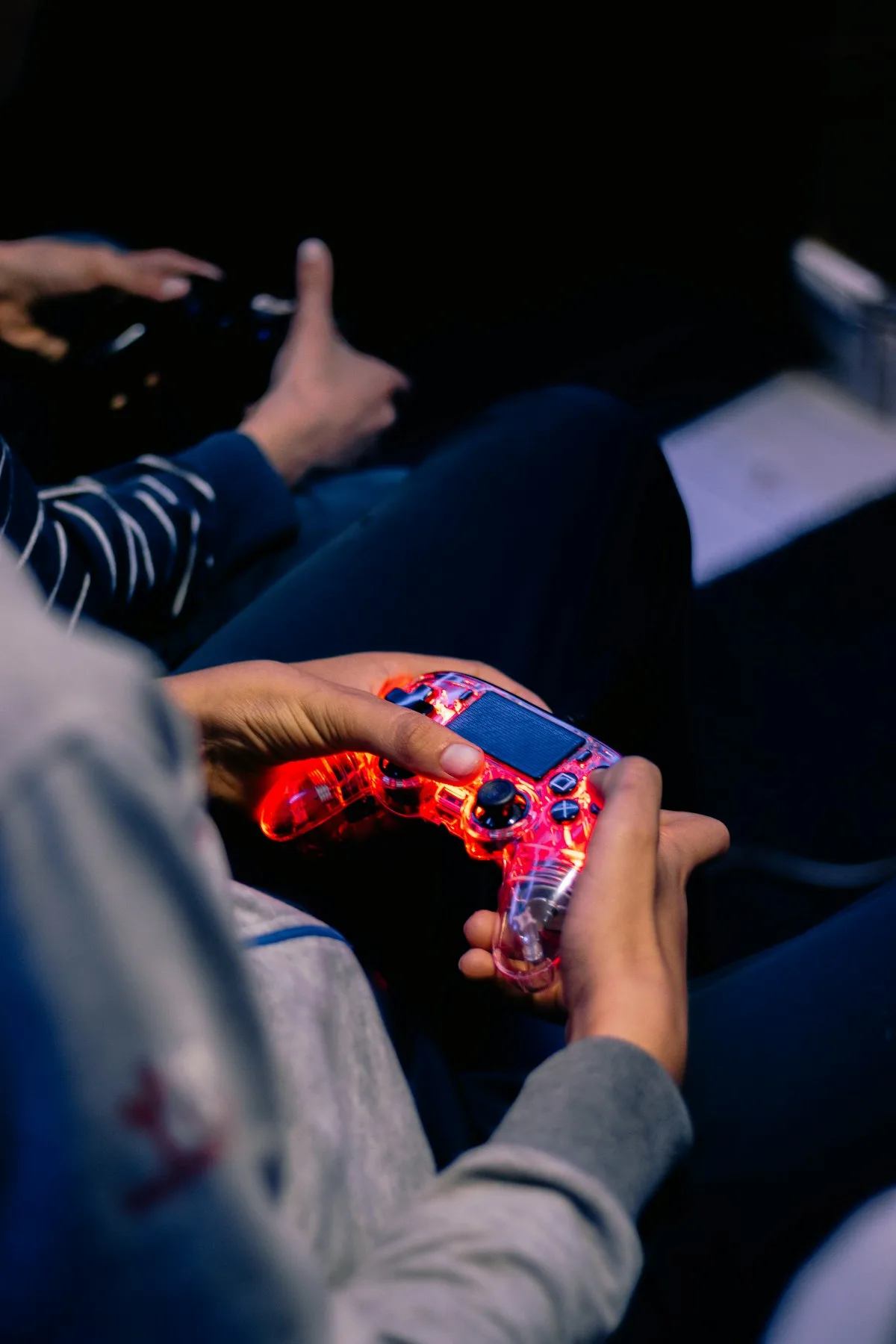 Two people sitting close together, playing a video game with illuminated controllers in a dark room
