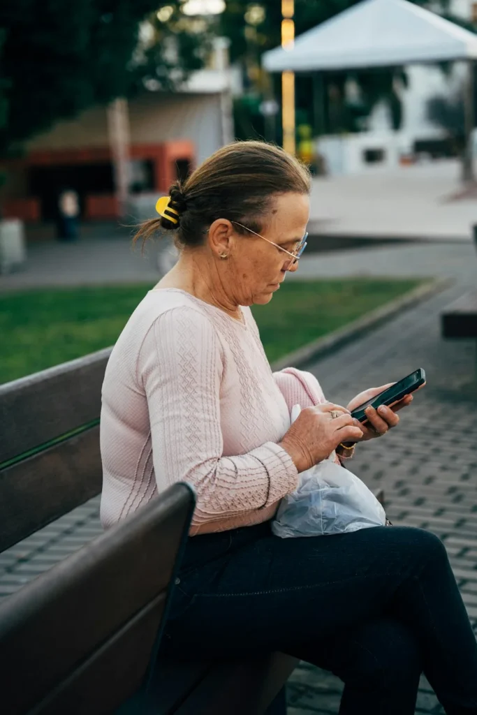 A woman sitting alone on a park bench, looking down at her phone