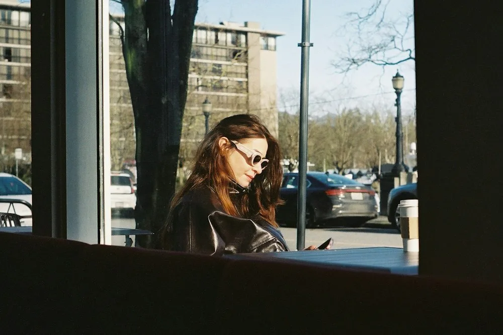 A woman sitting alone in a cafe, looking down at her phone