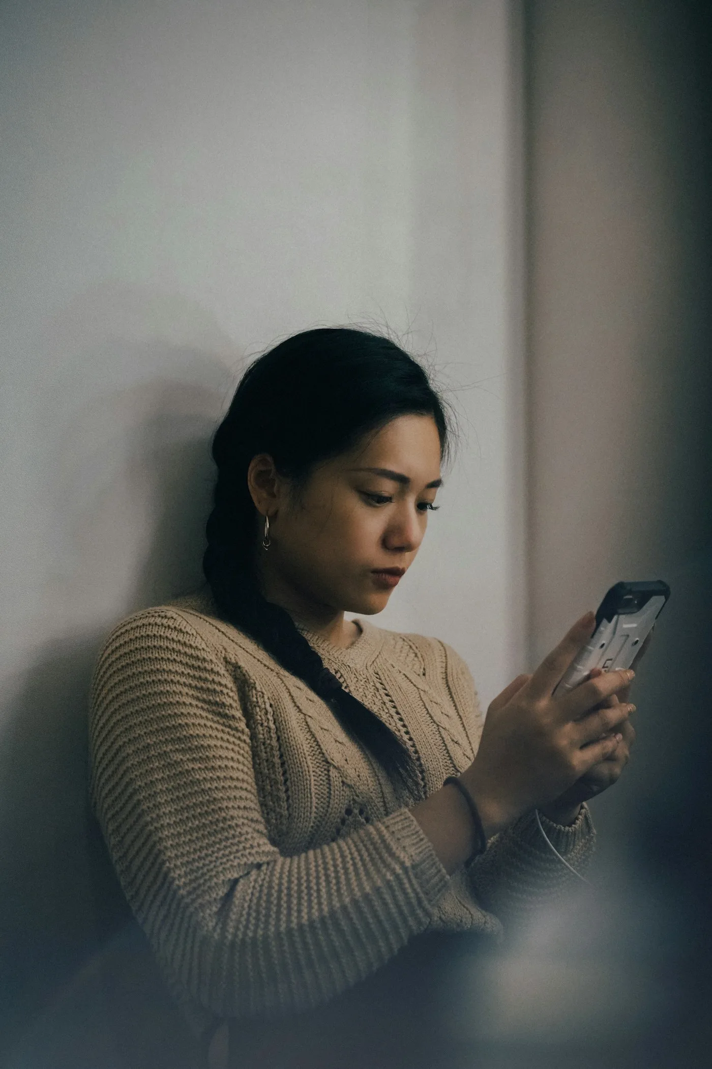 Woman leaning against a wall in natural daylight, looking at her phone