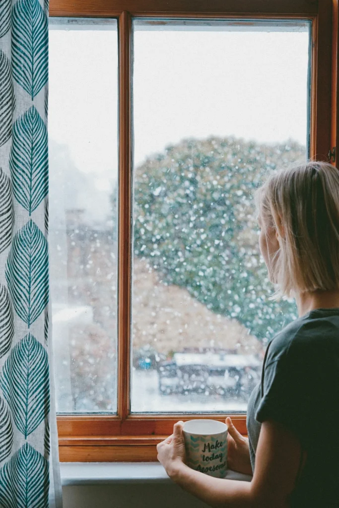 A woman holding a mug and looking out a rainy window