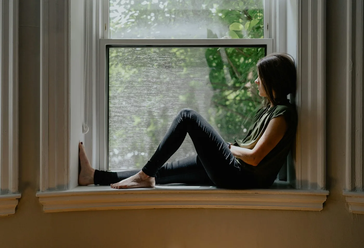 A woman sitting in a sunlit window sill, looking out