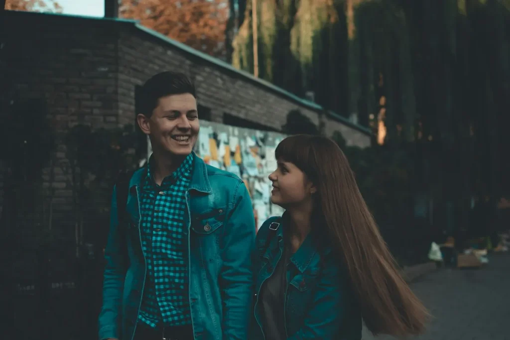 A young couple in denim jackets smiling at each other on a city street