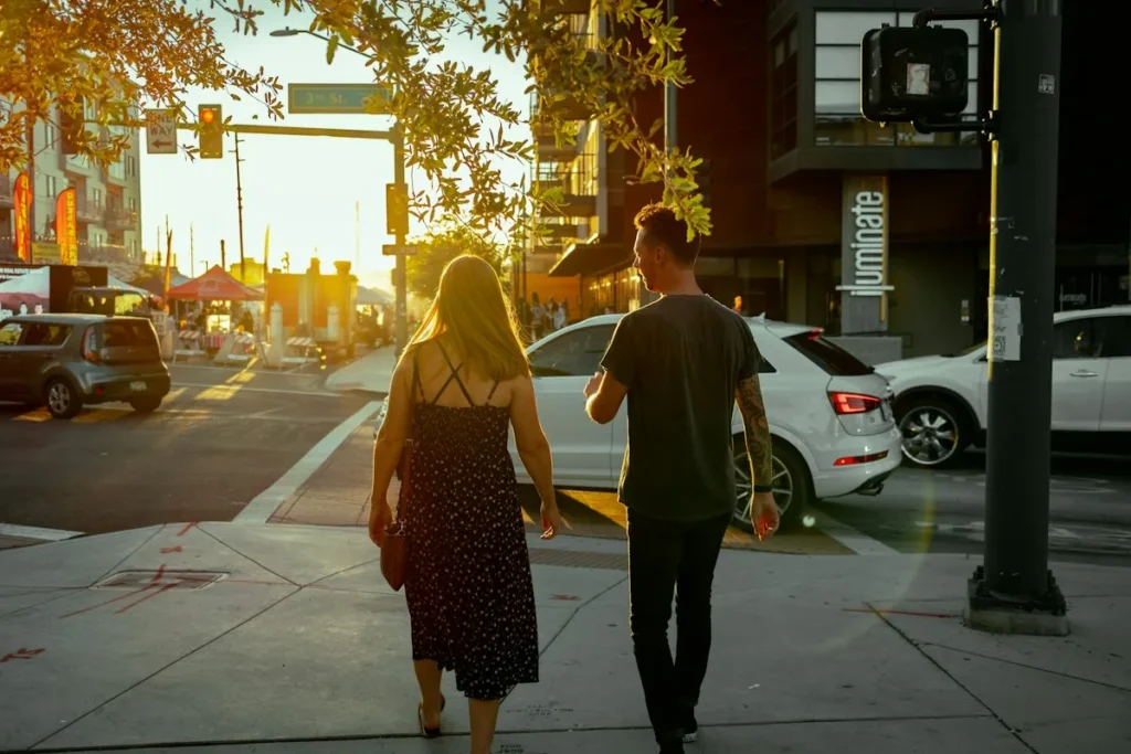 A young couple walking down a city street together in golden-hour light, seen from behind