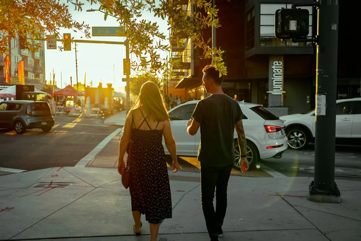 A young couple walking down a city street together in golden-hour light, seen from behind