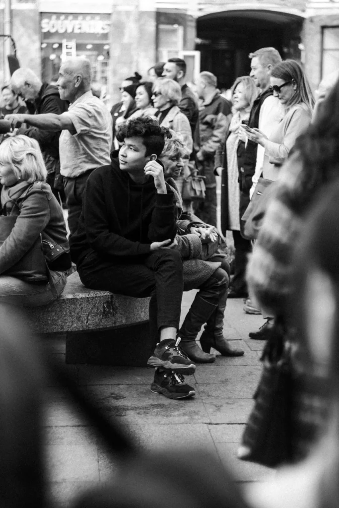A young person sitting apart, visibly separate within a crowd of people