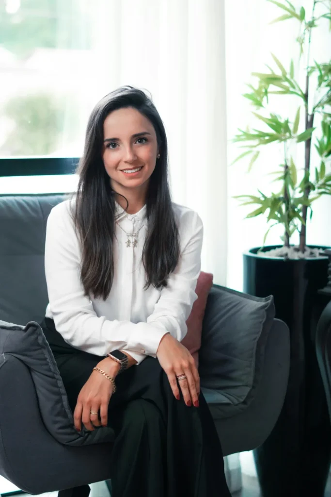 Una profesional sonriendo, sentada en un sillón en un consultorio luminoso con una planta al fondo