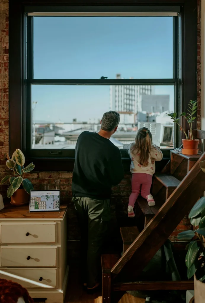 Un hombre y una niña pequeña mirando juntos por una ventana