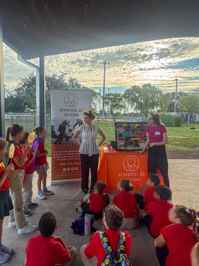 Behavioral Aid Solutions team members at their station with a feelings board and roll-up banner as students gather under an outdoor pavilion at Palm Springs North K-8 Center
