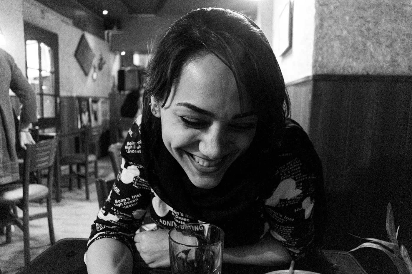 Una mujer sonriendo con la mirada baja en un caf&eacute;, en blanco y negro